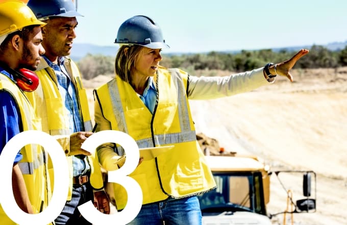 Construction workers and engineers wearing safety vests and hard hats at a worksite, with a female supervisor giving instructions.