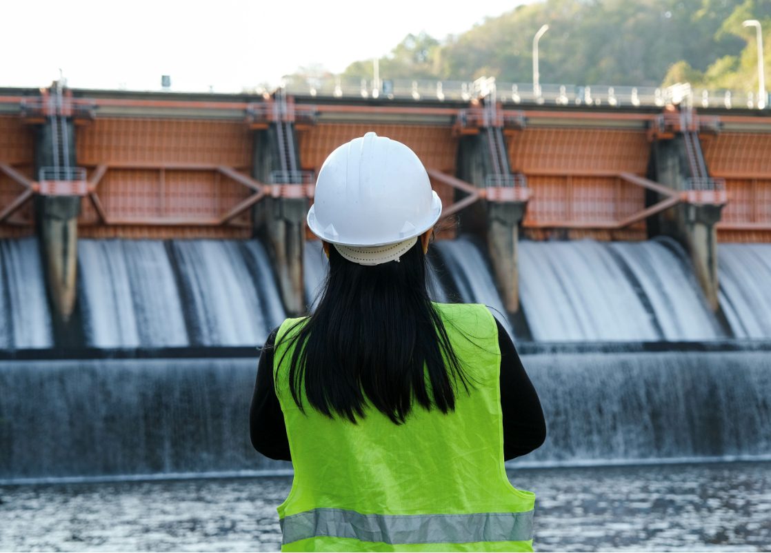 Female engineer wearing a hard hat and safety vest inspecting a hydroelectric dam, demonstrating Powertech services in renewable energy infrastructure, water resource management, and sustainable power generation.